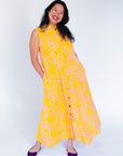 Model wearing yellow sleeveless dress with abstract pink print.