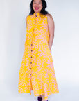 Model wearing yellow sleeveless dress with abstract pink print.