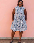 Model wearing white sleeveless dress with blue floral print.