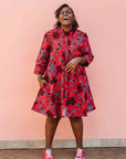 Model wearing red dress with floral vine print.
