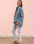 Model wearing green, blue, black squiggle print, long sleeved blouse, paired with jeans and tan flats.
