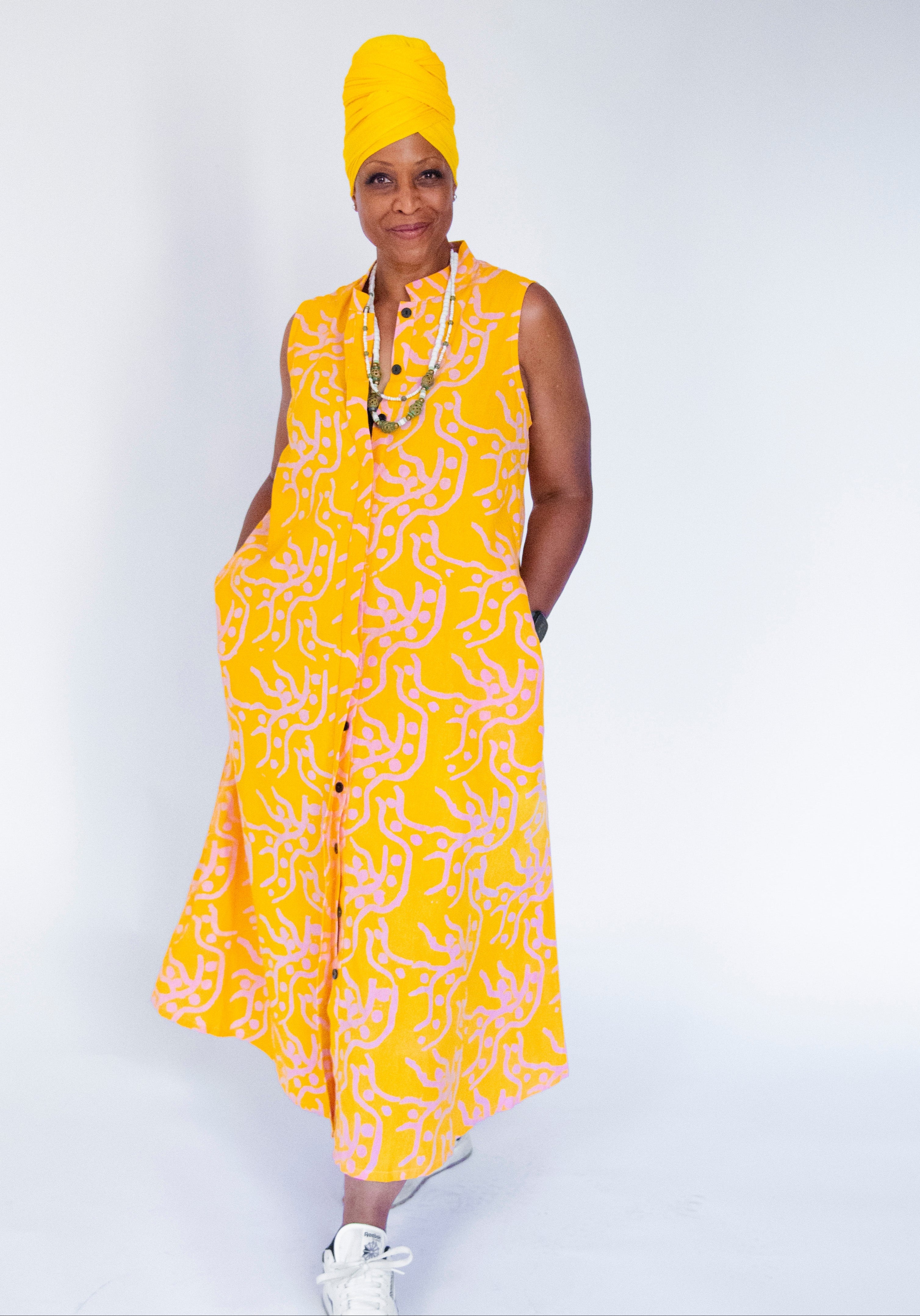 Model wearing yellow sleeveless dress with abstract pink print.