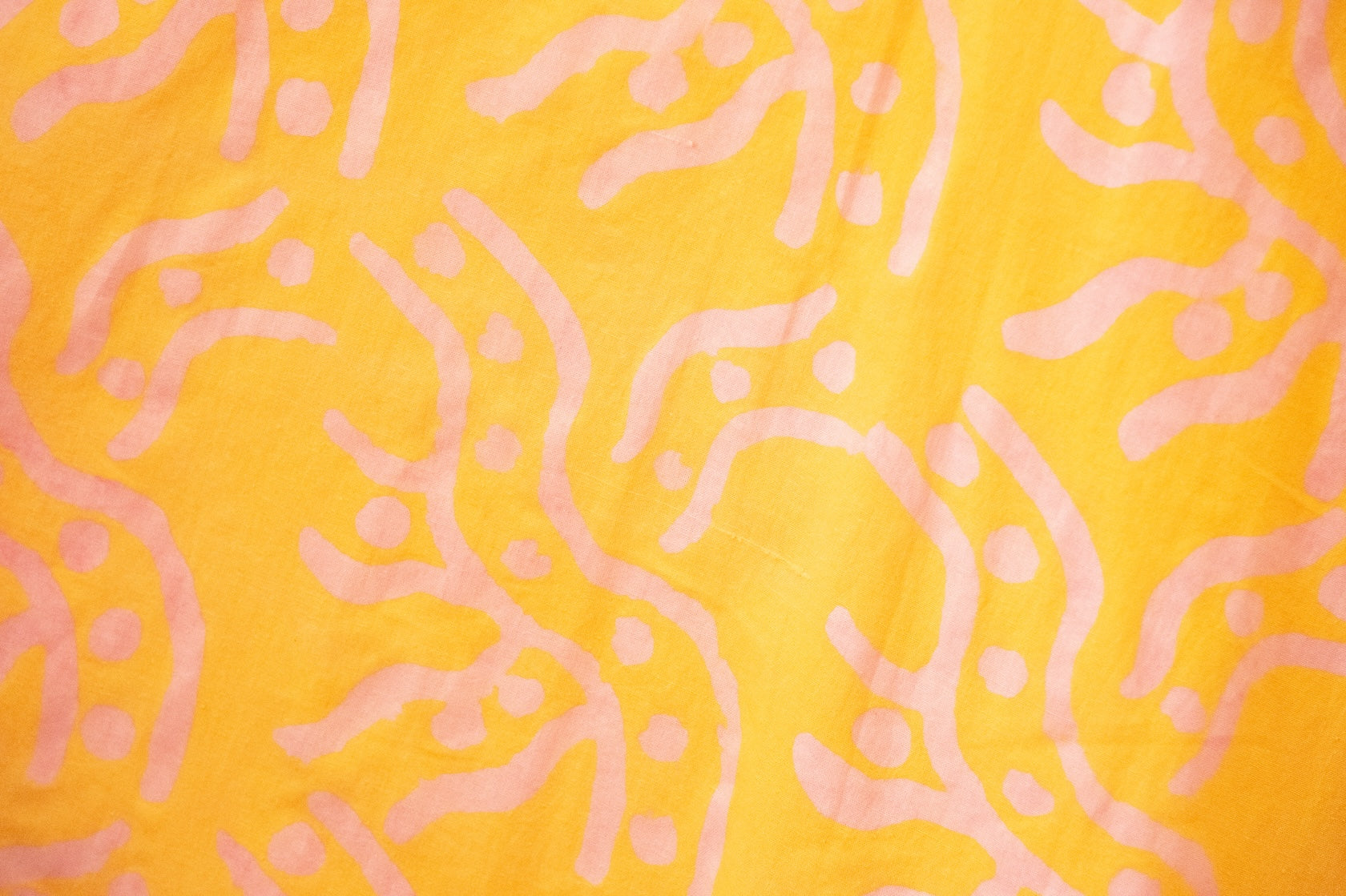 Close up display of yellow sleeveless dress with abstract pink print, fabric.