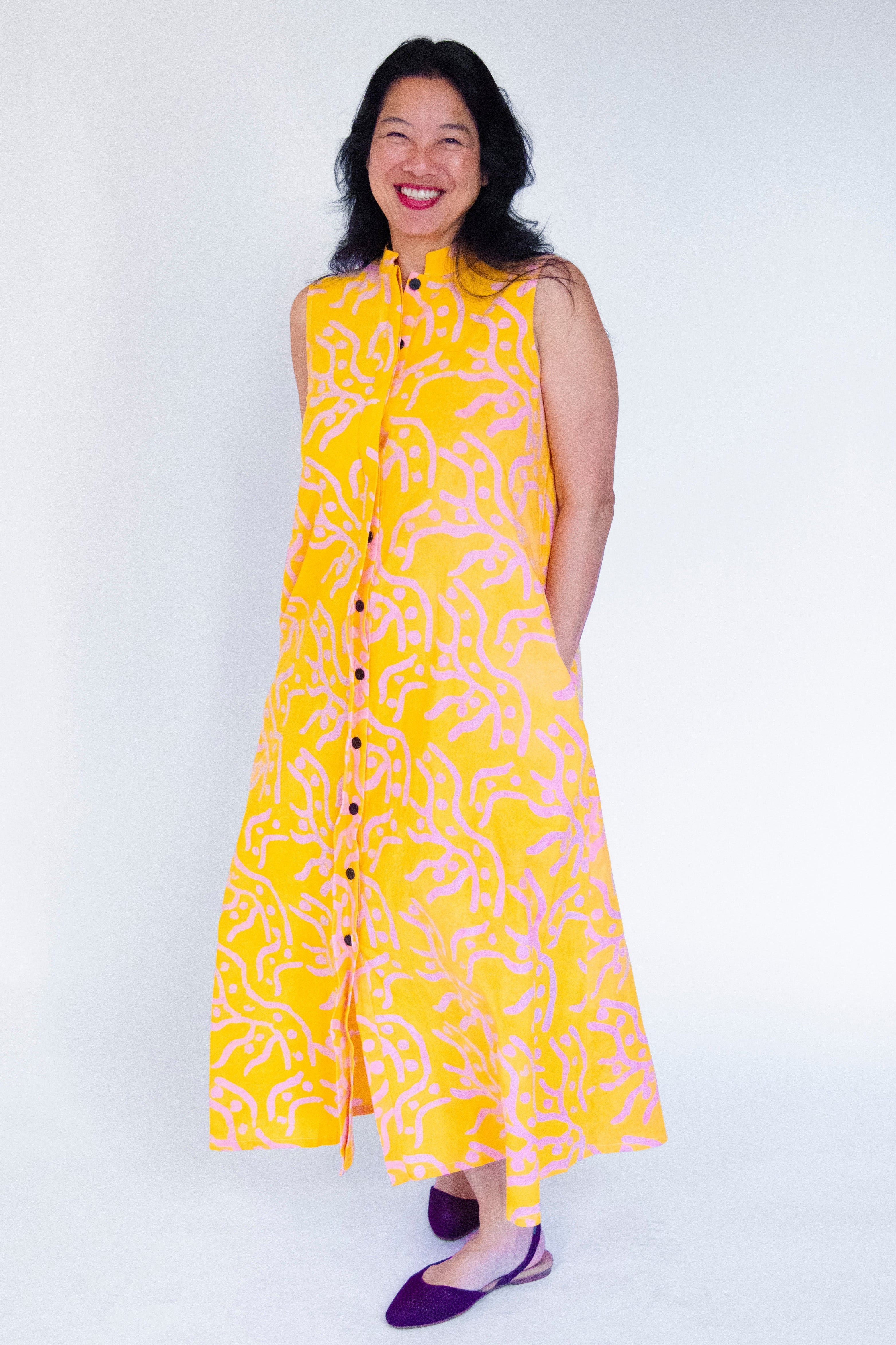 Model wearing yellow sleeveless dress with abstract pink print.