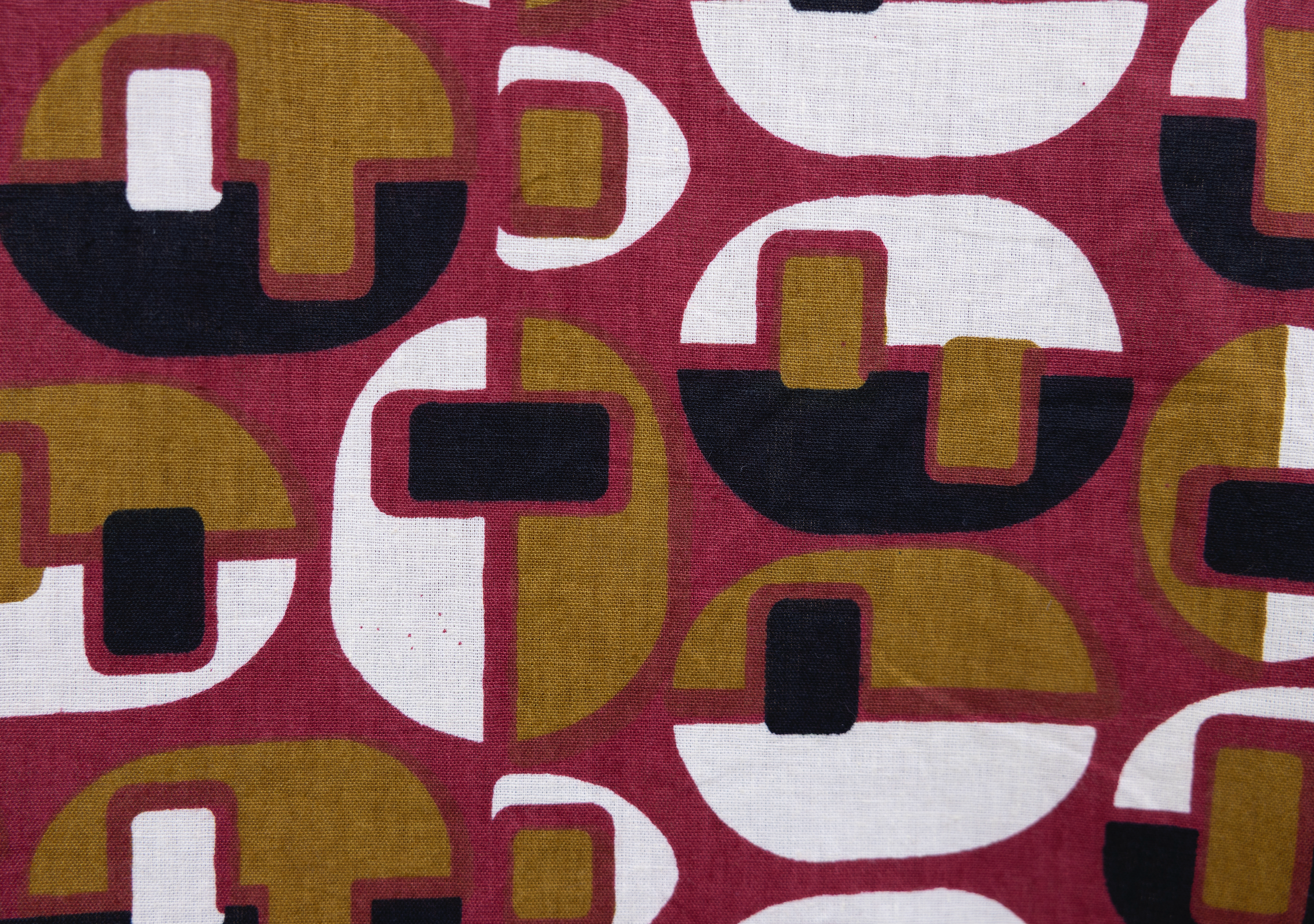 Close up display of burgundy, mustard and black geometric print dress, fabric.