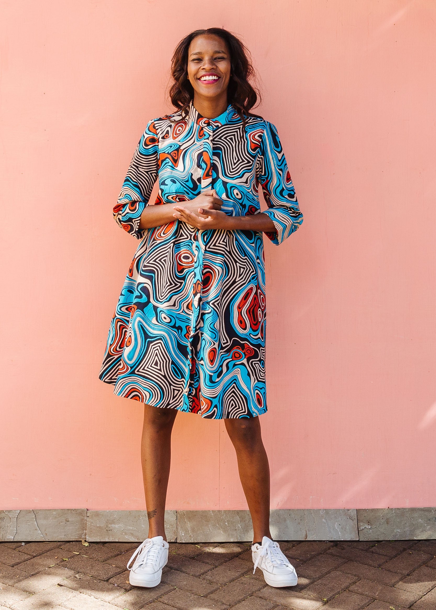 Model wearing beige, orange, navy and aqua, abstract print dress.