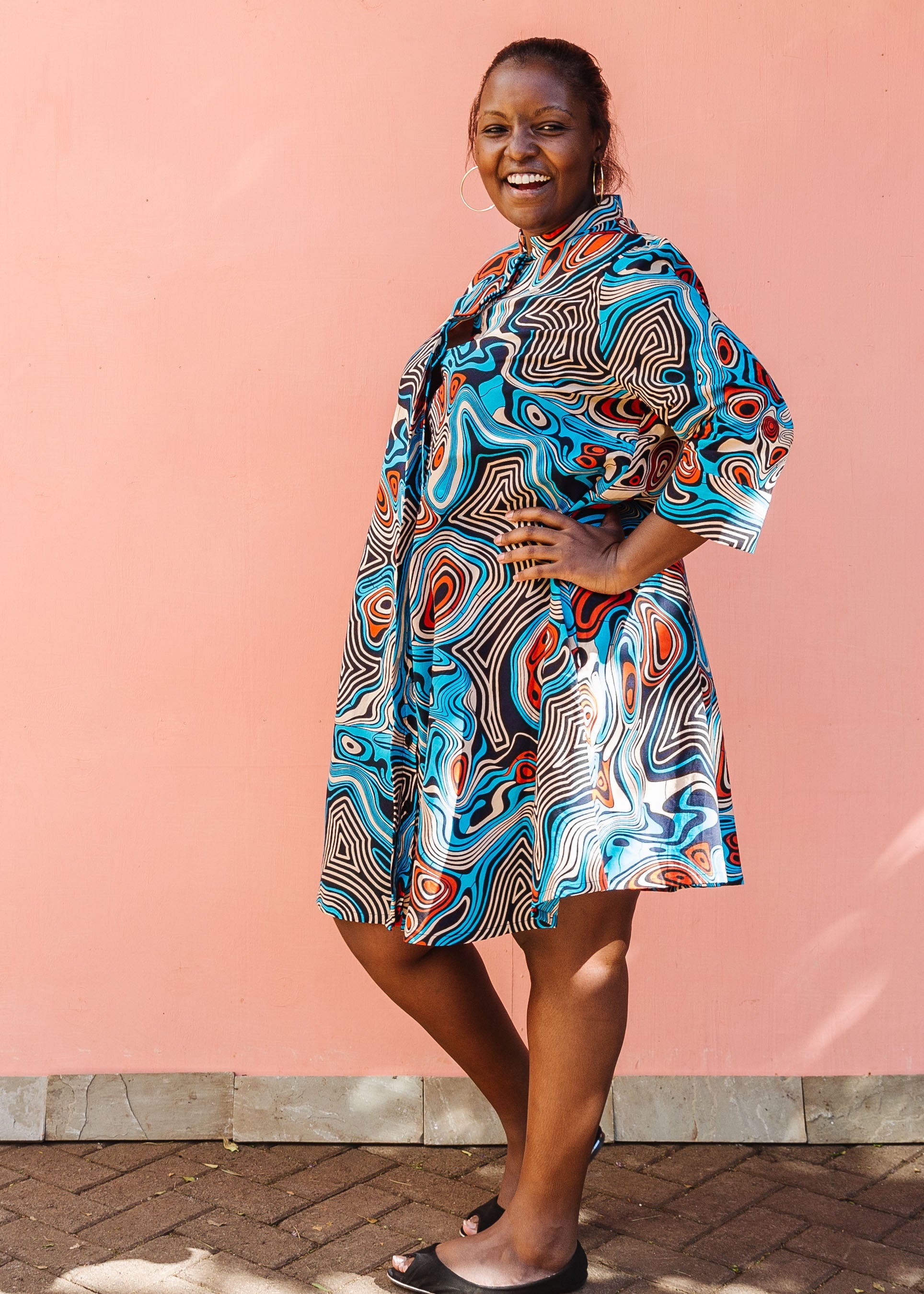 Model wearing beige, orange, navy and aqua, abstract print dress.