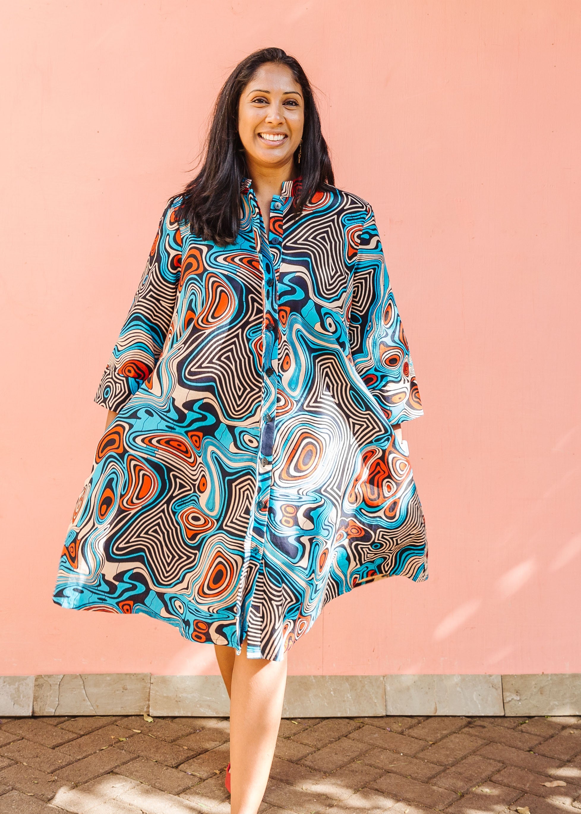 Model wearing beige, orange, navy and aqua, abstract print dress.