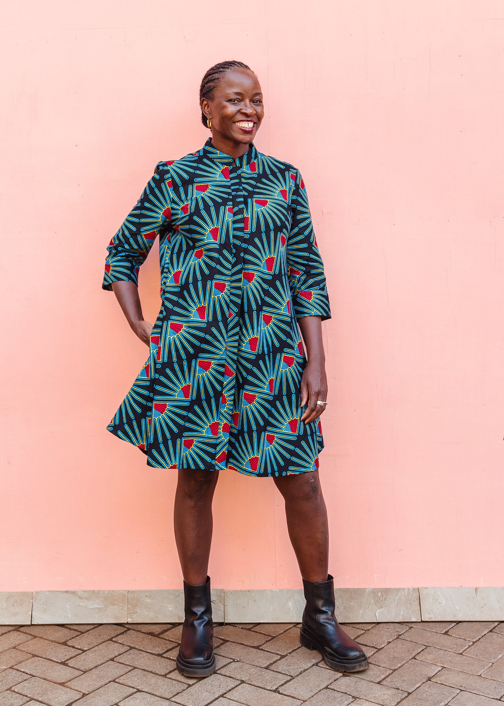 Model wearing black dress with blue, red and yellow fan design, paired with black boots.