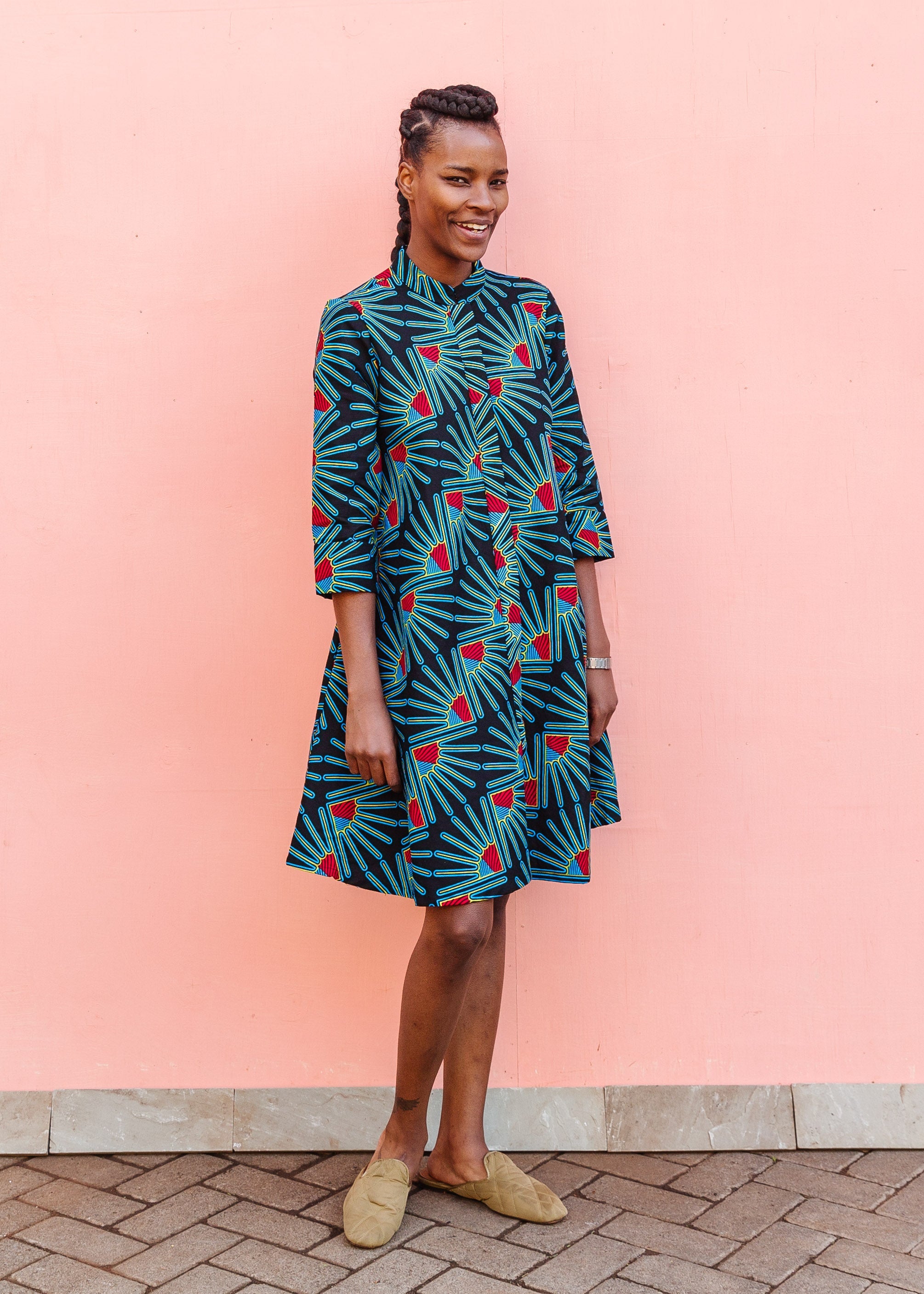 Model wearing black dress with blue, red and yellow fan design, paired with tan flats.