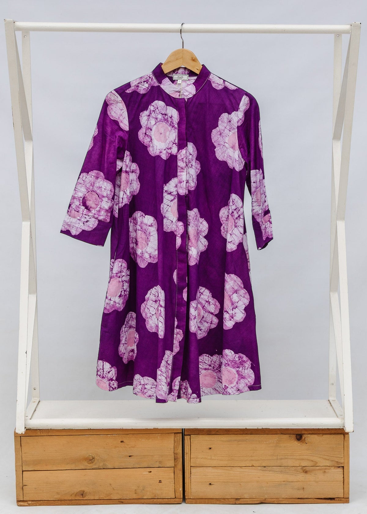 Purple dress with floral pattern on a wooden rack against a white background