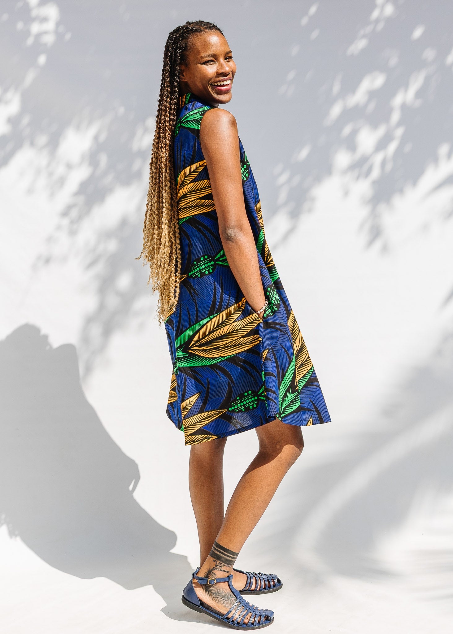 Model wearing blue sleeveless dress with orange and green print.