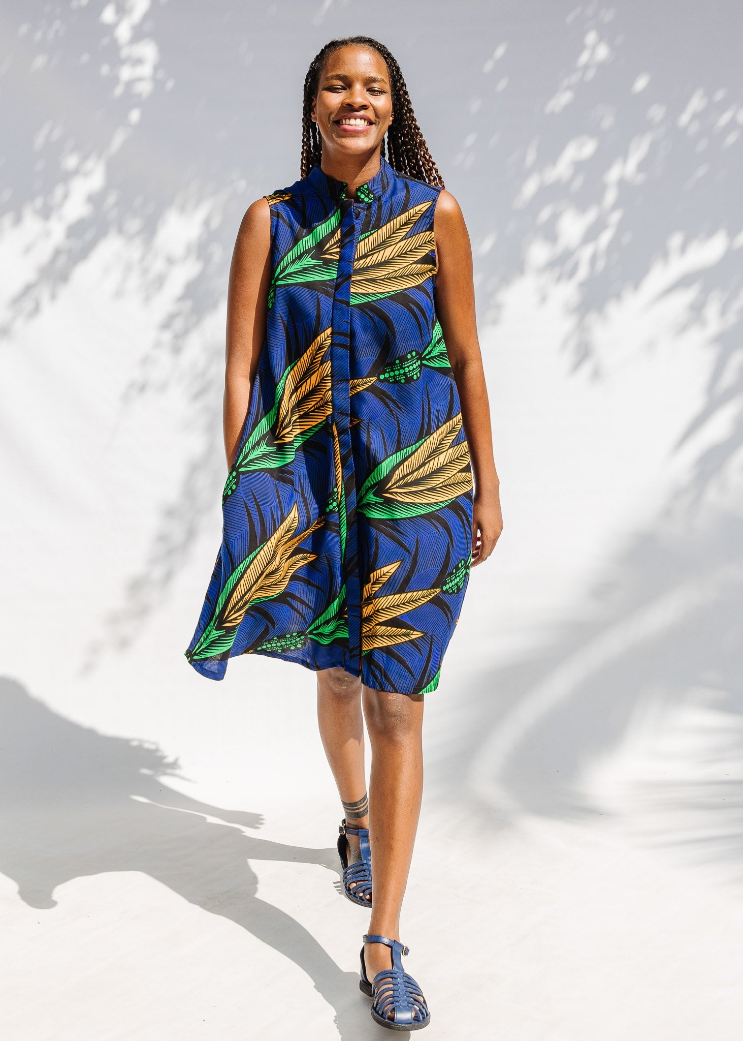 Model wearing blue sleeveless dress with orange and green print.