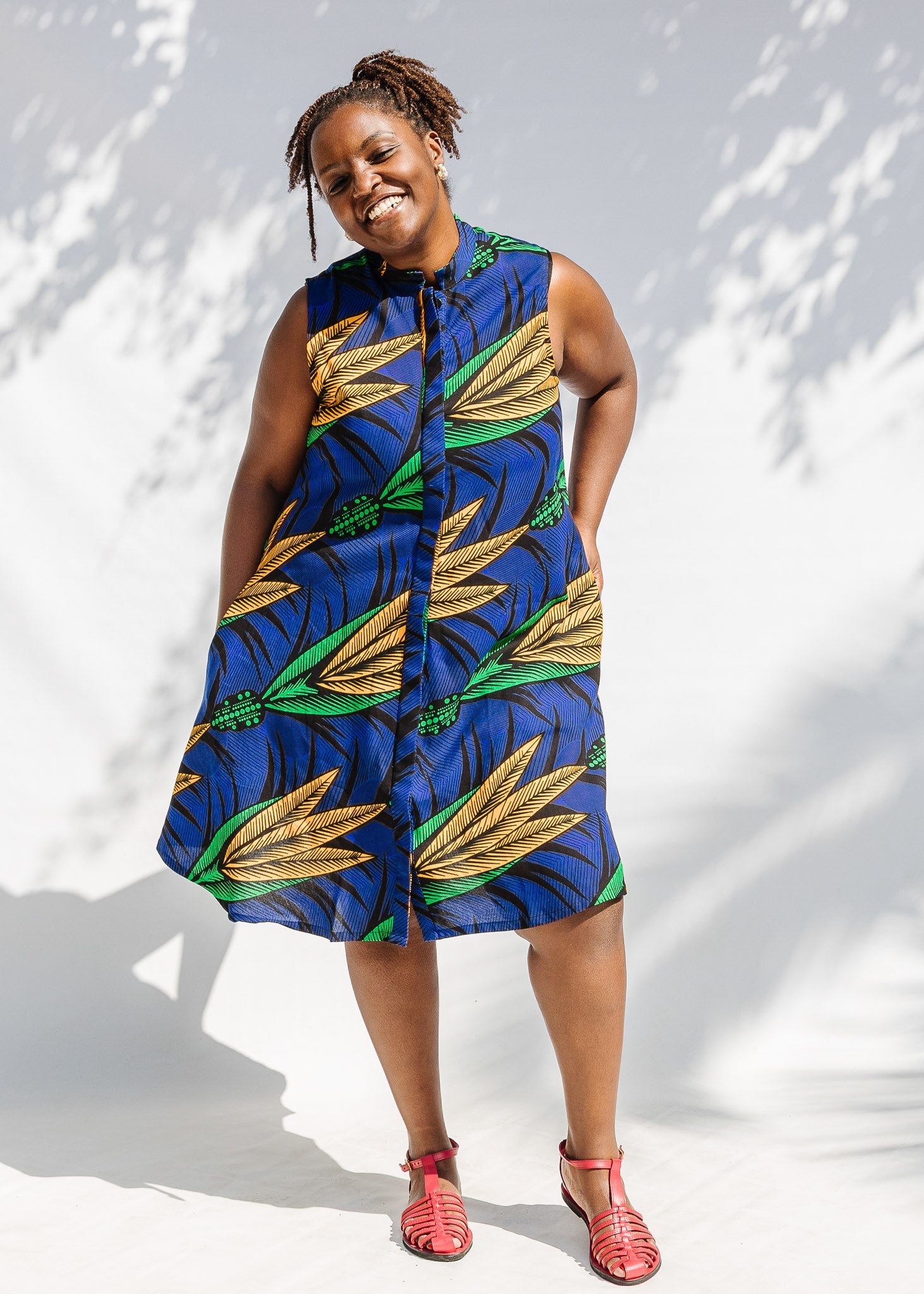 Model wearing blue sleeveless dress with orange and green print.