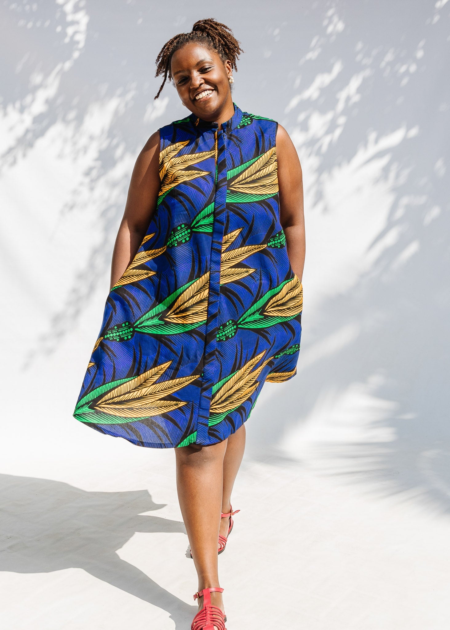 Model wearing blue sleeveless dress with orange and green print.