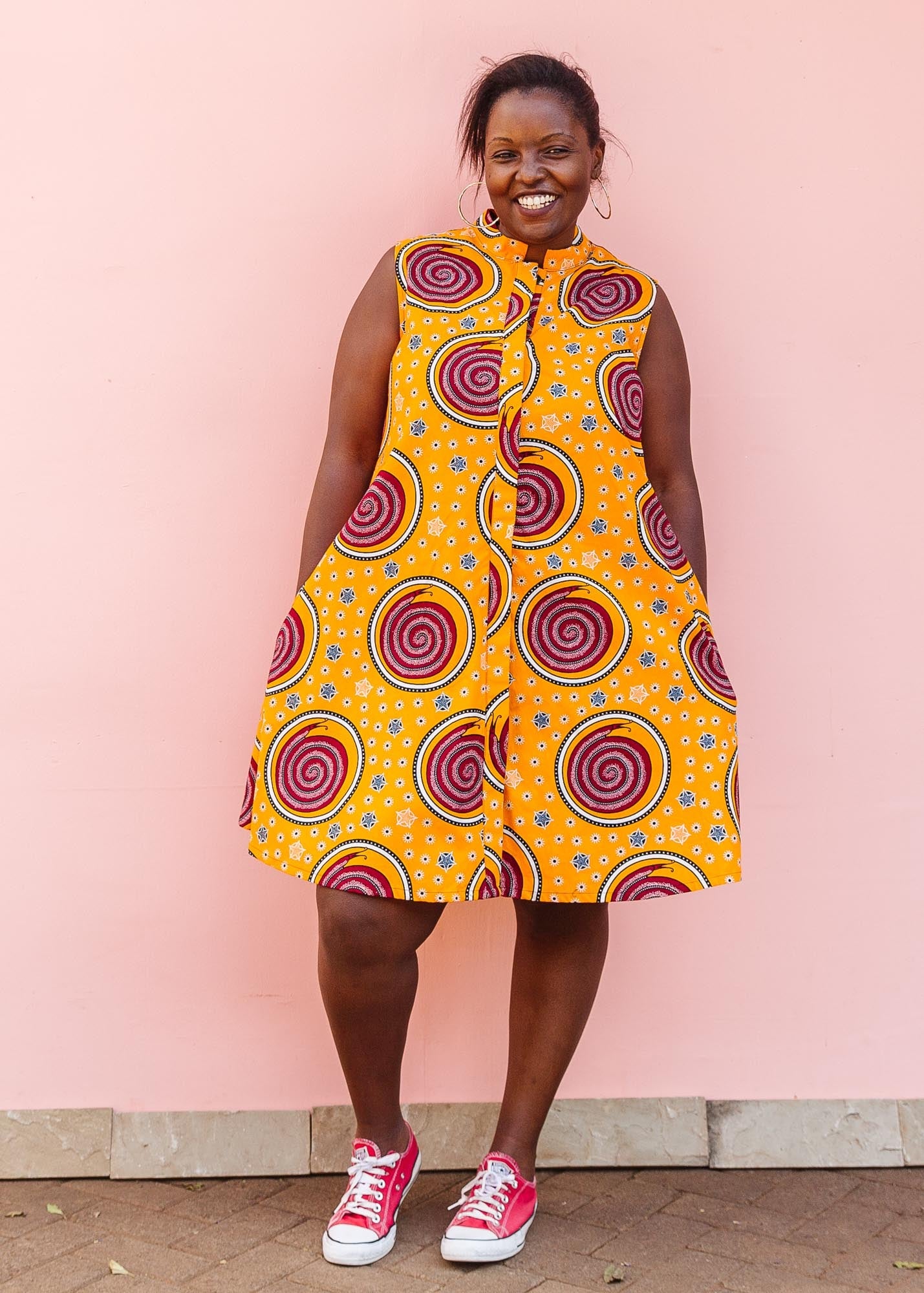 The model is wearing orange white, black and burgundy snail design dress