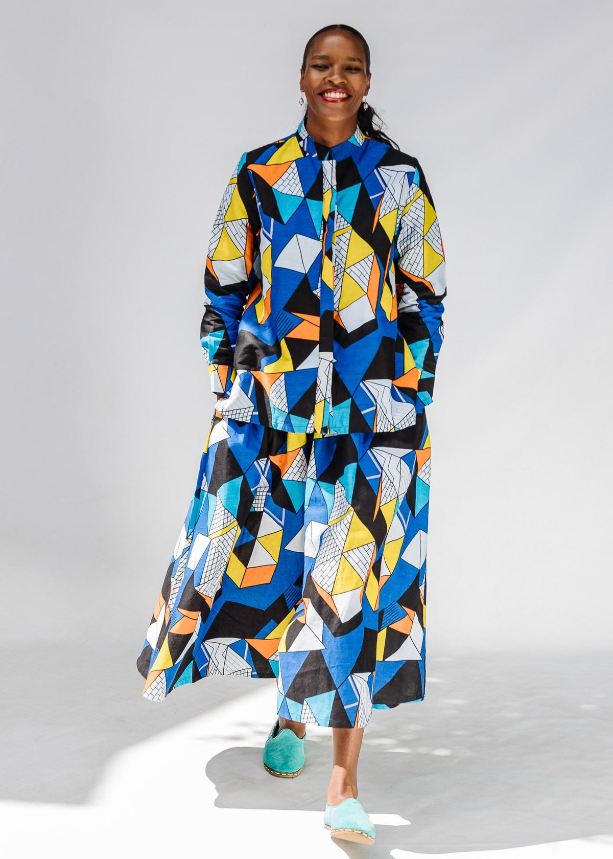 Model wearing blue, black, orange, yellow and white geometric print shirt and pant set.