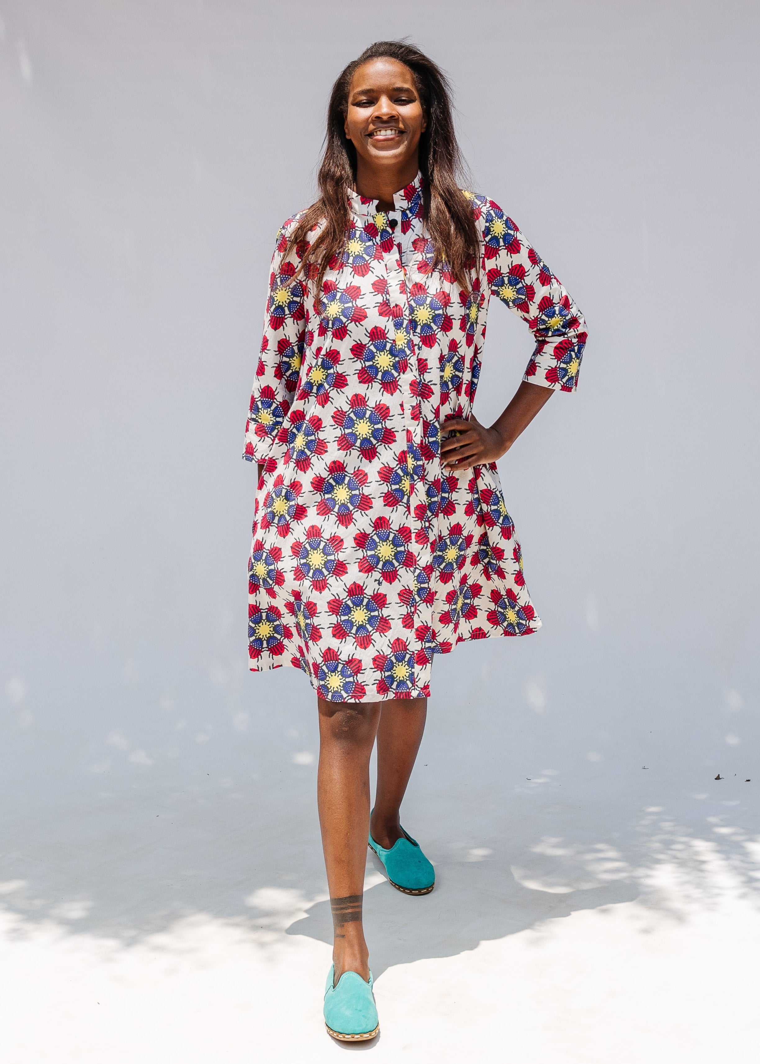Model wearing white dress with yellow, red and blue bug print.