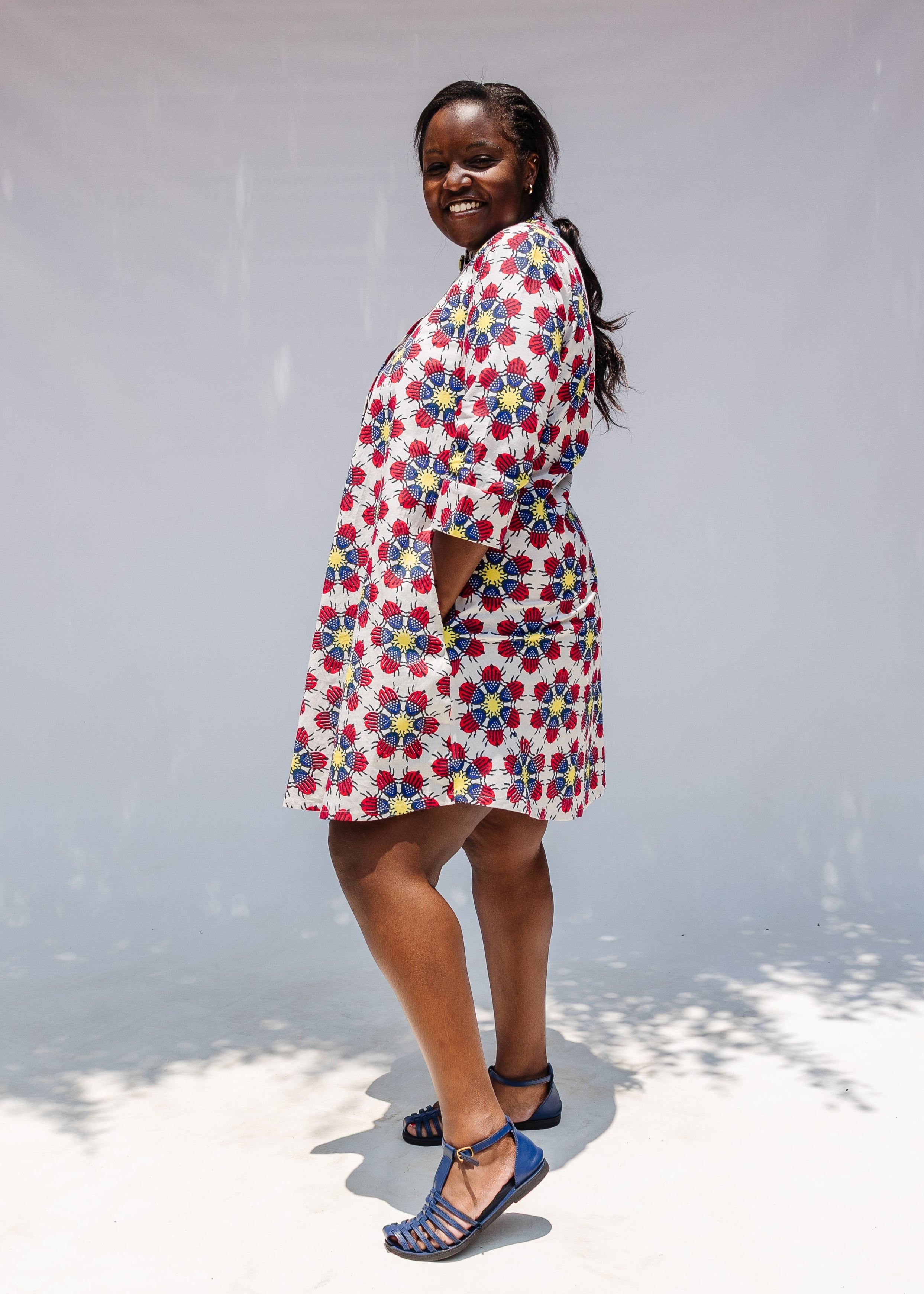 Model wearing white dress with yellow, red and blue bug print.