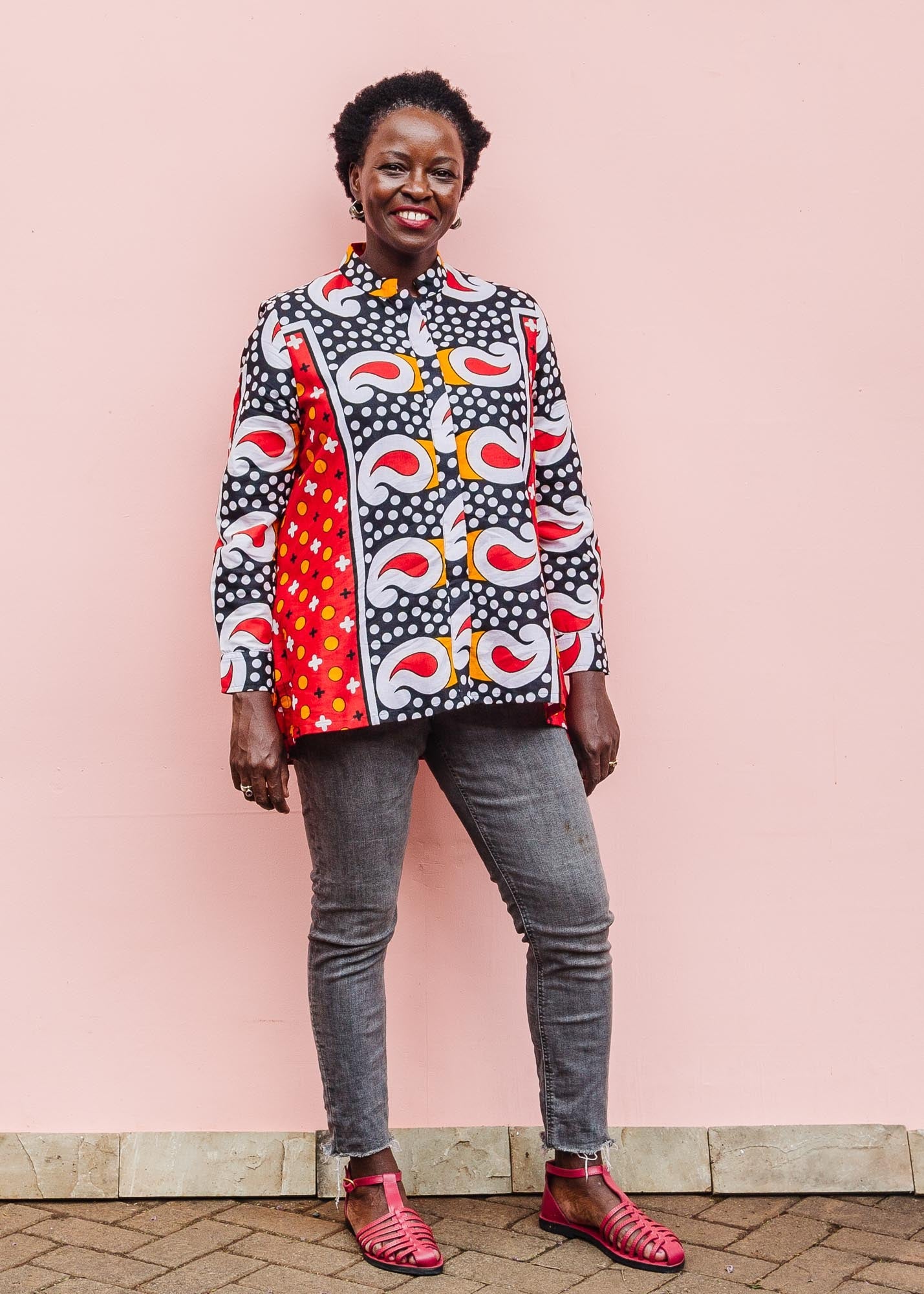 The model is wearing red, white, black and orange mixed pattern long sleeved kanga shirt