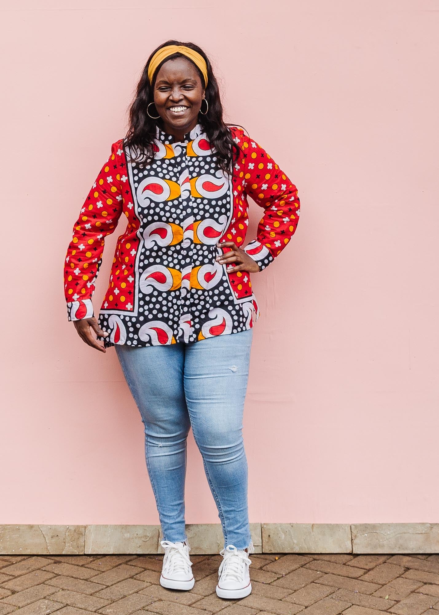 The model is wearing red, white, black and orange mixed pattern long sleeved kanga shirt