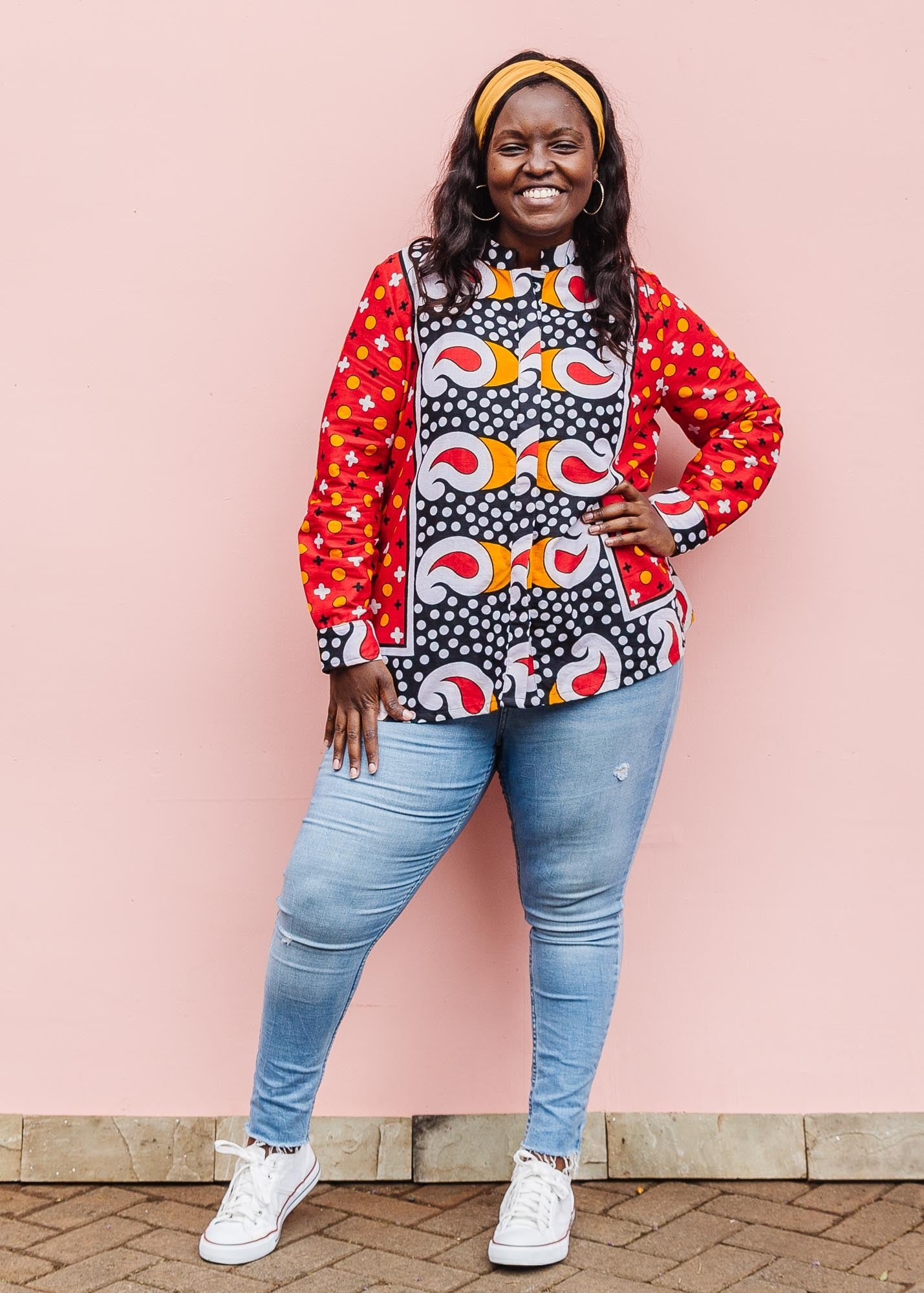 The model is wearing red, white, black and orange mixed pattern long sleeved kanga shirt
