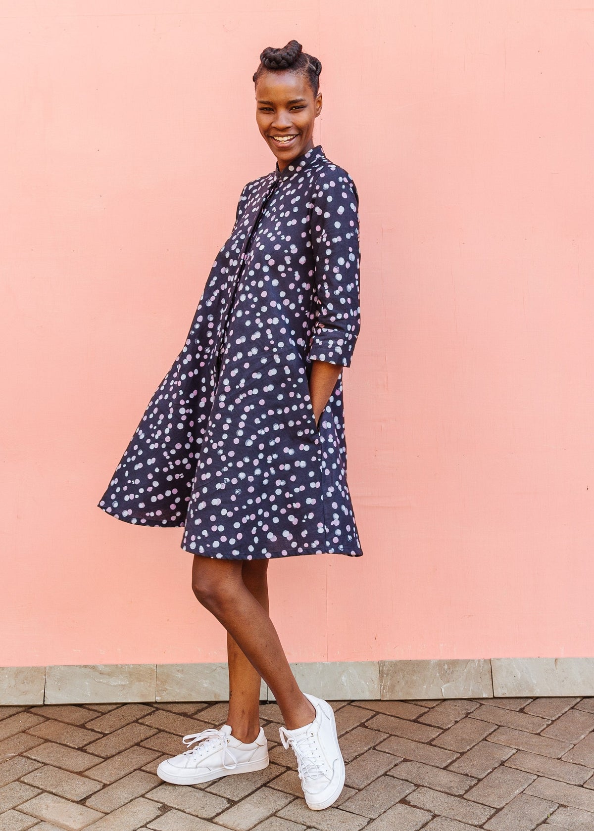 Model wearing black dress with pink and white polka dots, paired with white sneakers.