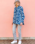 Model wearing blue batik shirt with white domino print, paired with gray jeans and white sneakers.