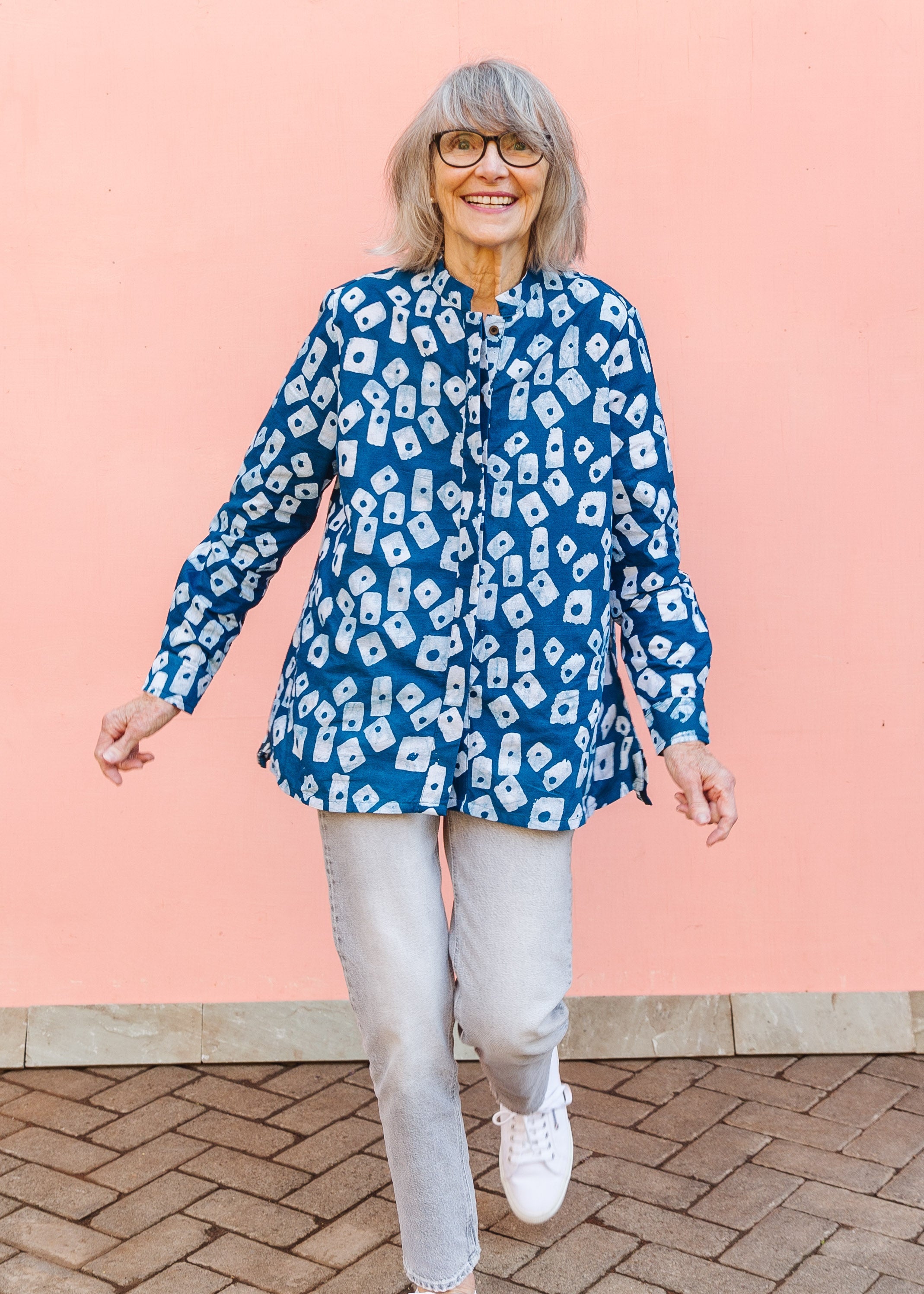 Model wearing blue batik shirt with white domino print, paired with gray jeans and white sneakers.