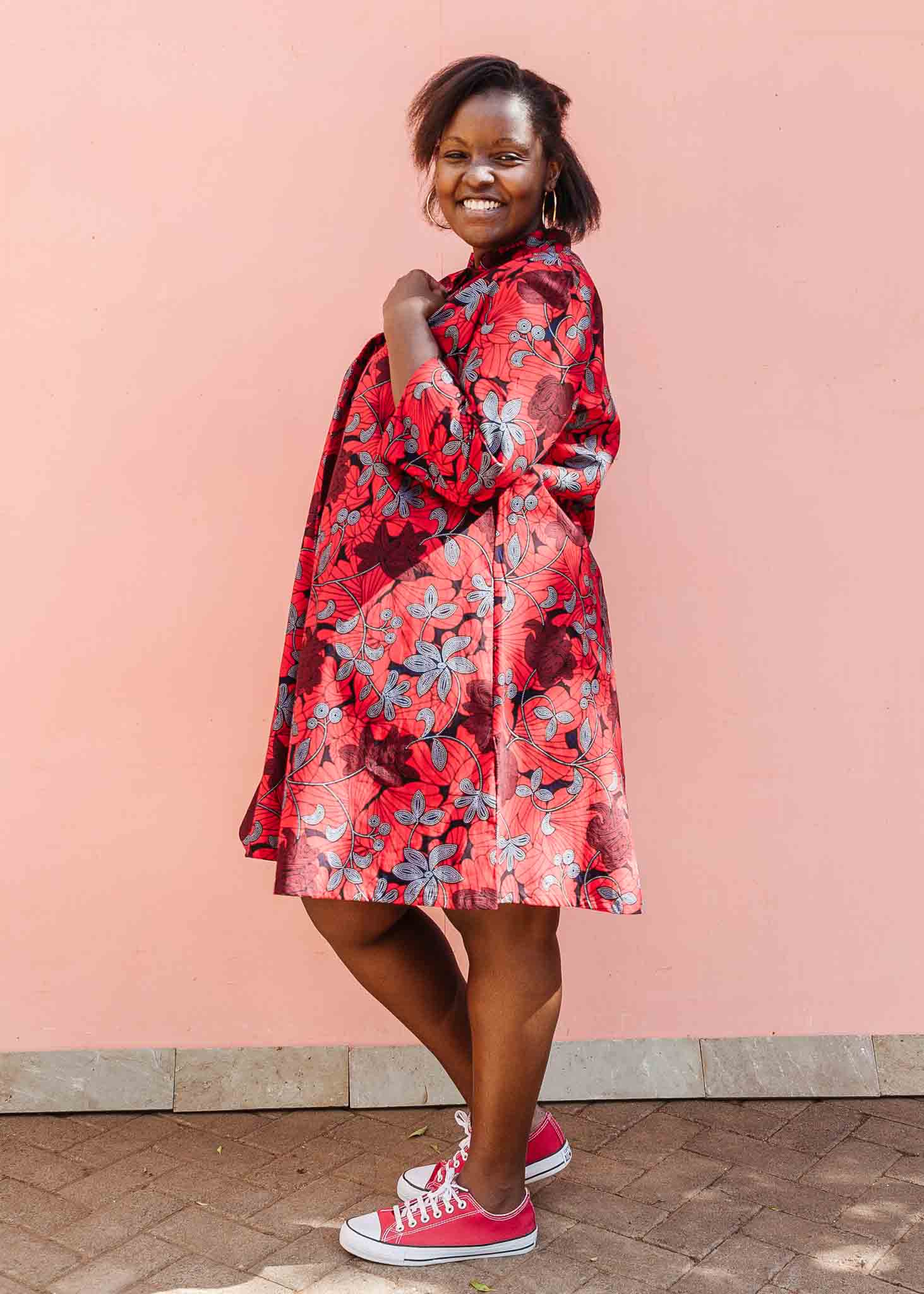 Model wearing red dress with floral vine print.