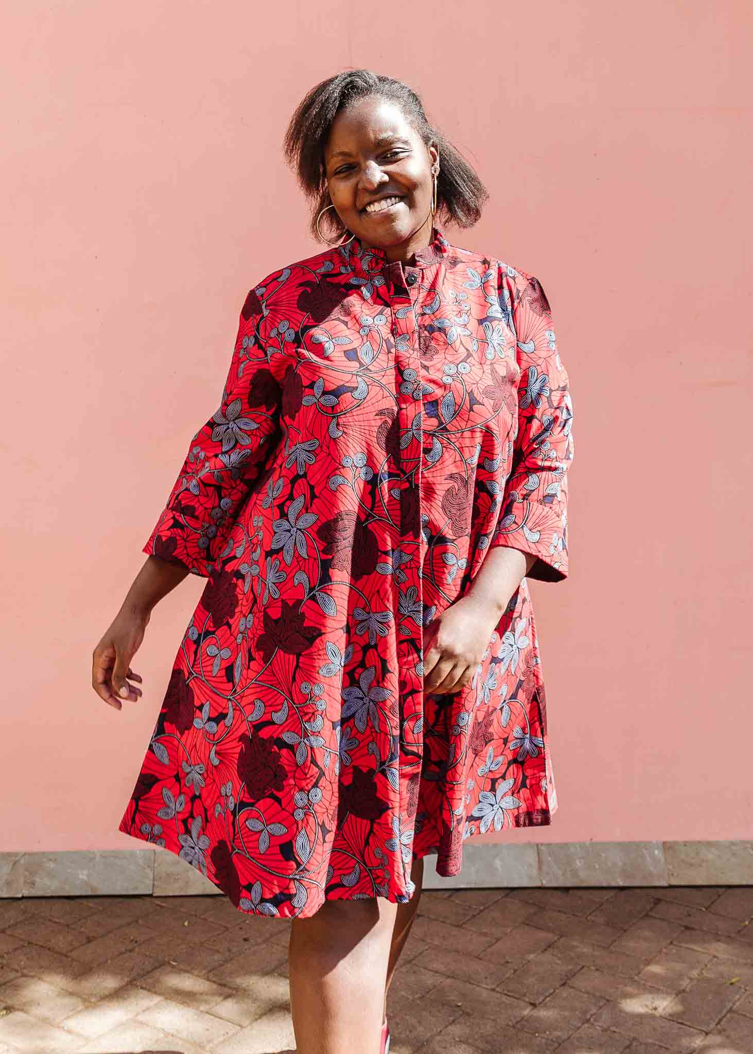 Model wearing red dress with floral vine print.
