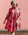Model wearing red dress with floral vine print.