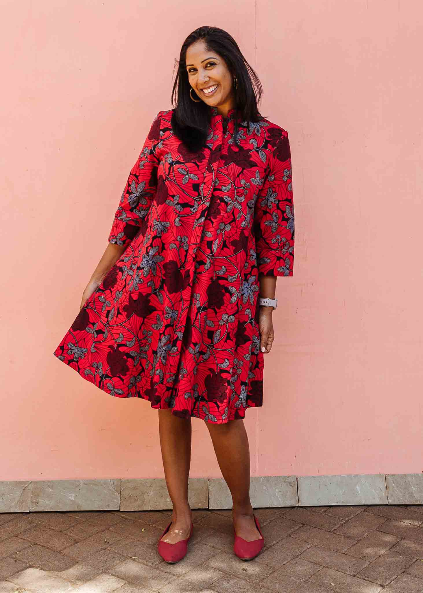 Model wearing red dress with floral vine print.