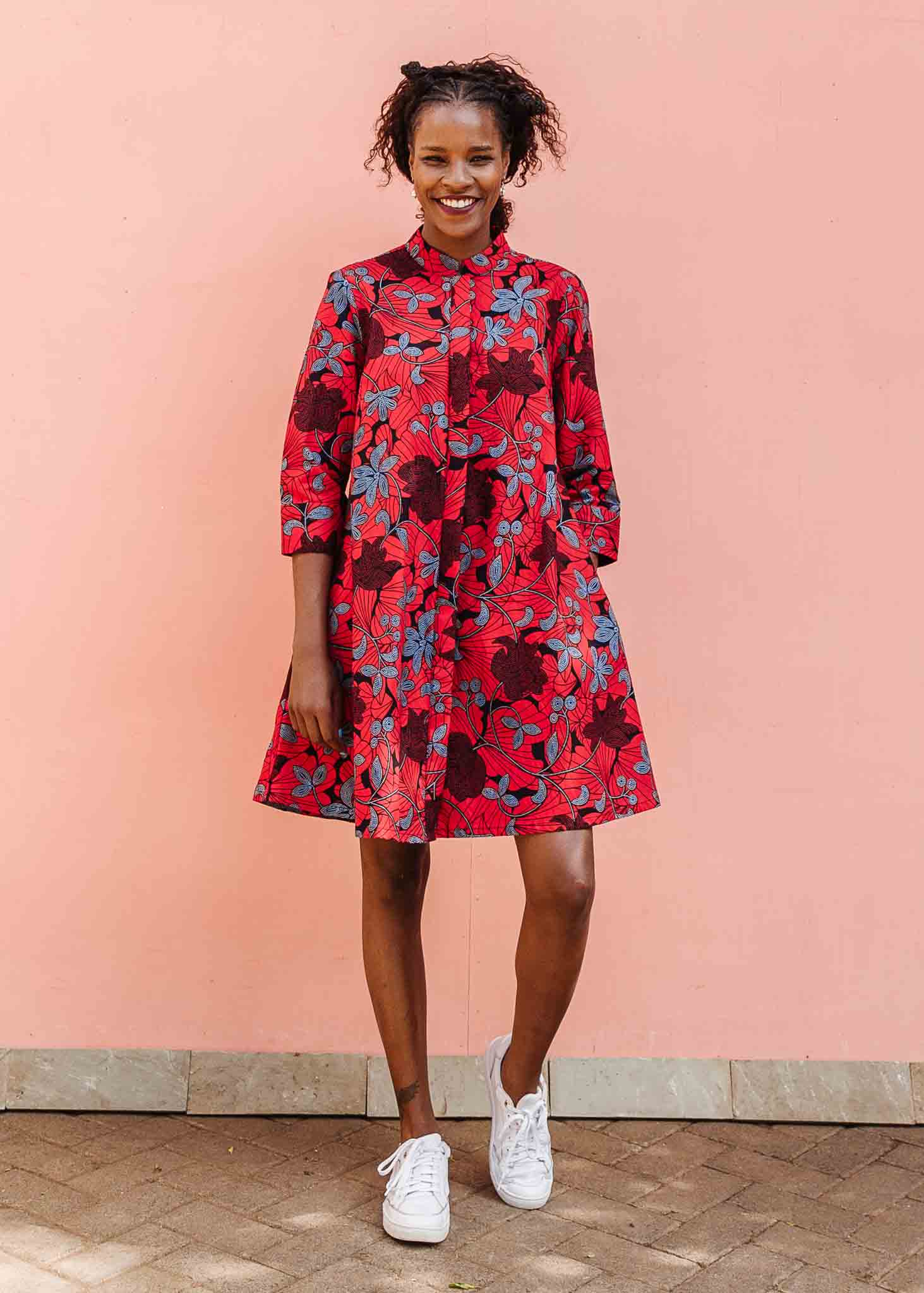 Model wearing red dress with floral vine print.
