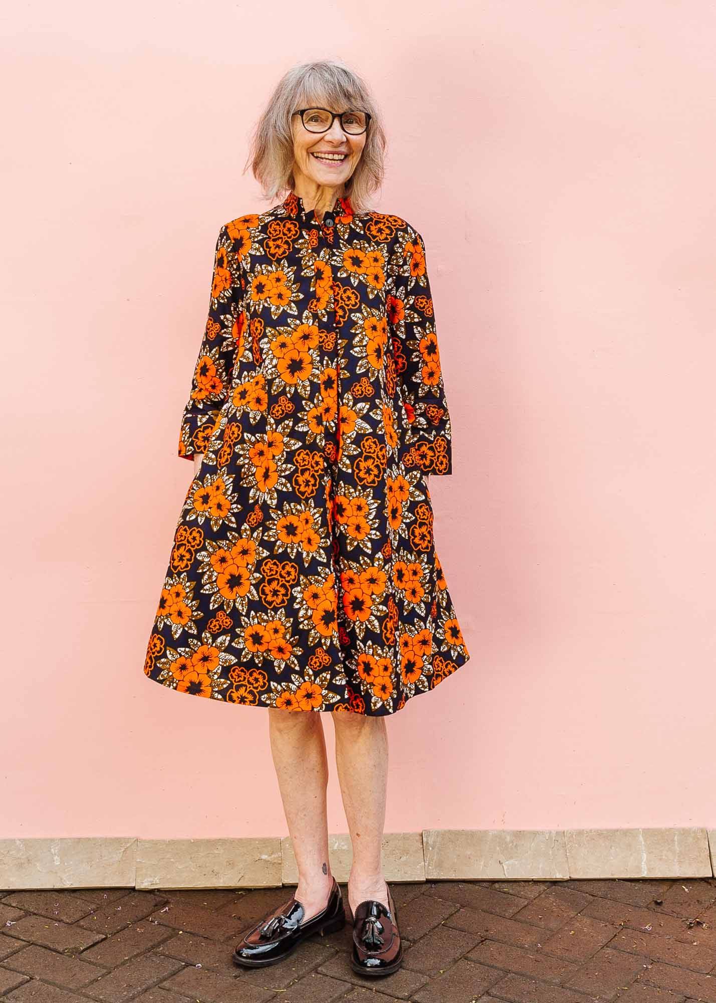 The model is wearing navy dress with orange, brown, black and white floral print