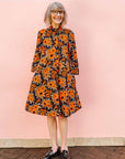 The model is wearing navy dress with orange, brown, black and white floral print