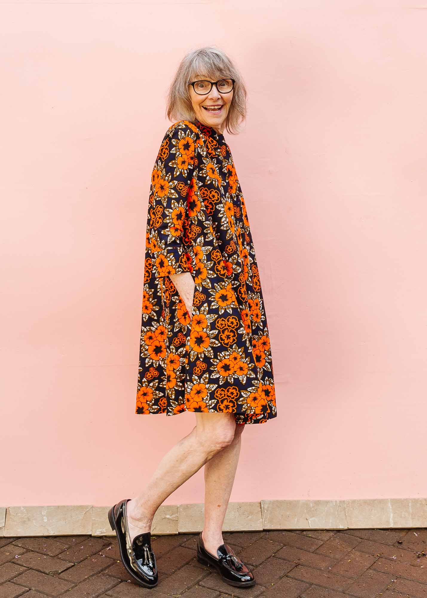 The model is wearing navy dress with orange, brown, black and white floral print