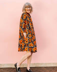 The model is wearing navy dress with orange, brown, black and white floral print