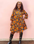 The model is wearing navy dress with orange, brown, black and white floral print