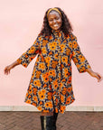 The model is wearing navy dress with orange, brown, black and white floral print