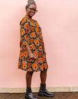 The model is wearing navy dress with orange, brown, black and white floral print