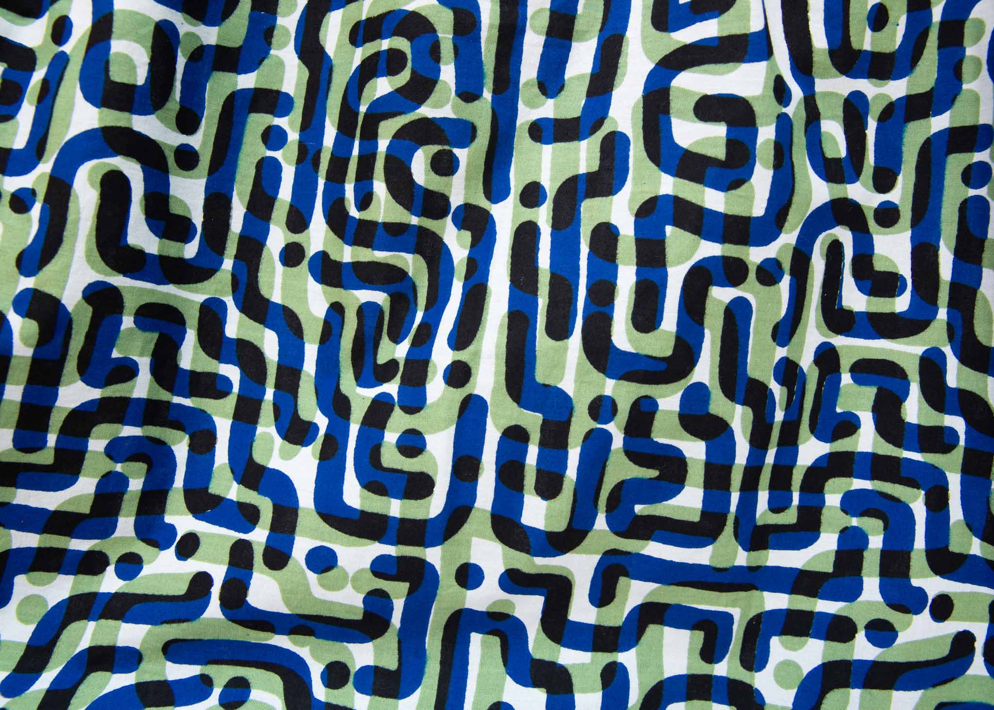 Close up of green, blue, black squiggle print, long sleeved blouse, fabric.