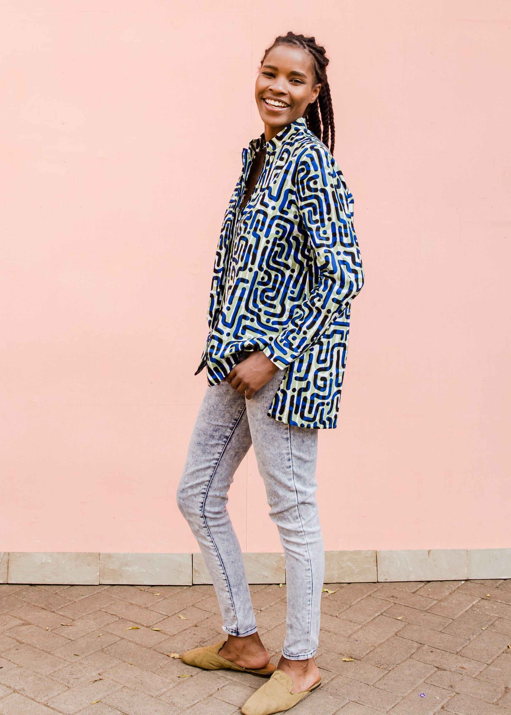 Model wearing green, blue, black squiggle print, long sleeved blouse, paired with jeans and tan flats.